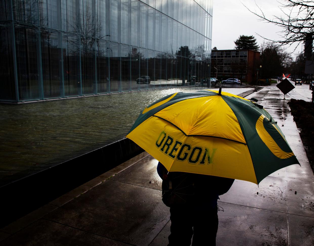 Rain falls on a gray day in Oregon as a passerby to the John E. Jaqua Center for Student Athletes on the University of Oregon campus shields himself from the elements.