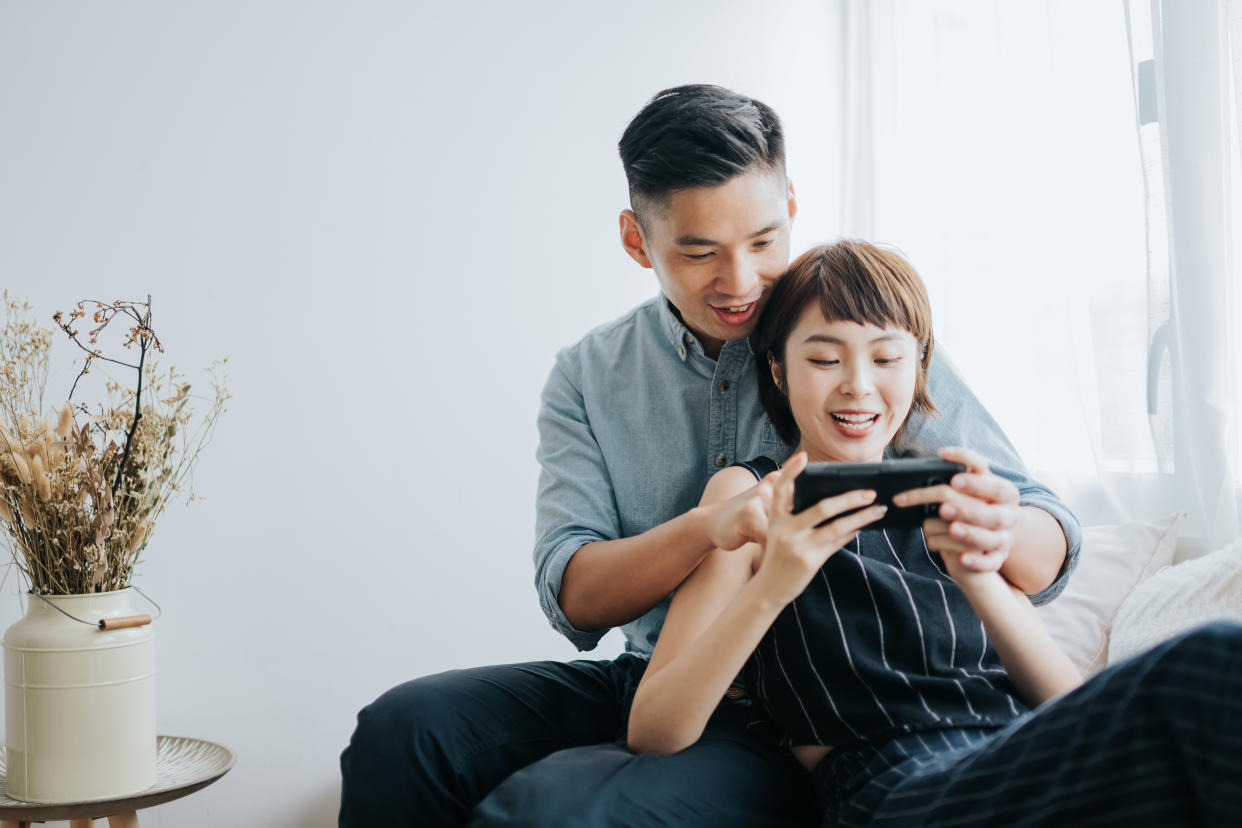 Happy young Asian couple sitting on a couch in the living room and playing video games with a game console