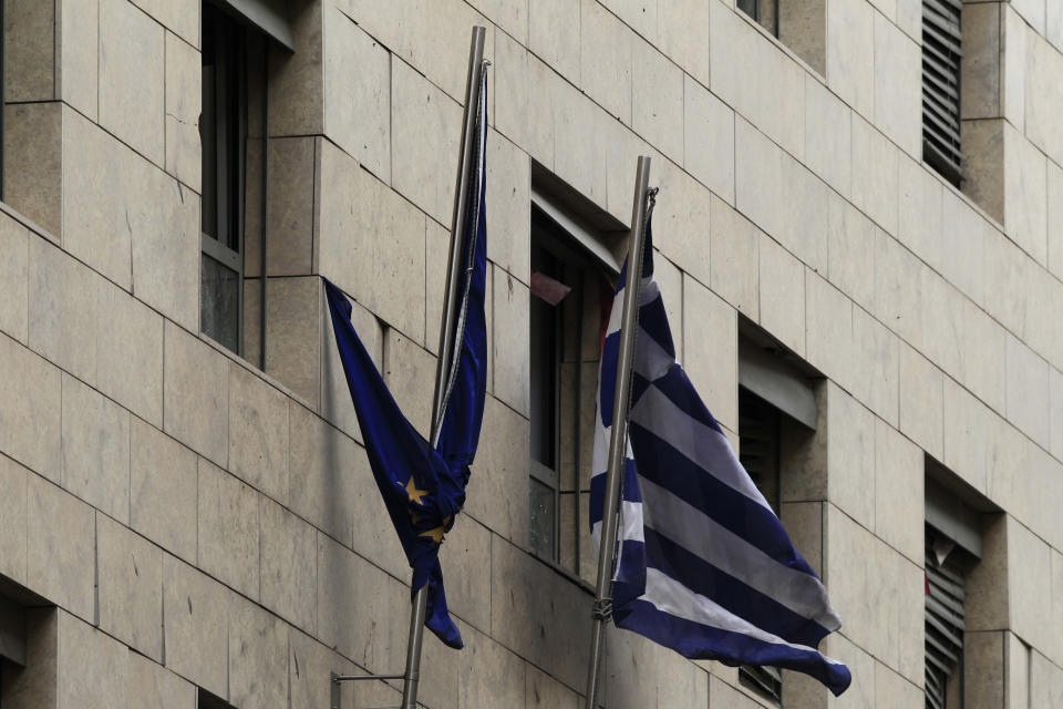 AN EU and a greek flag fly in front of broken windows of a Bank of Greece building Thursday, April 10, 2014. A bomb exploded outside a Bank of Greece building in central Athens before dawn Thursday, causing some damage but no injuries. The blast came hours before Greece was to return to the international bond markets for the first time in four years, and a day before German Chancellor Angela Merkel was to visit Athens. (AP Photo/Thanassis Stavrakis)