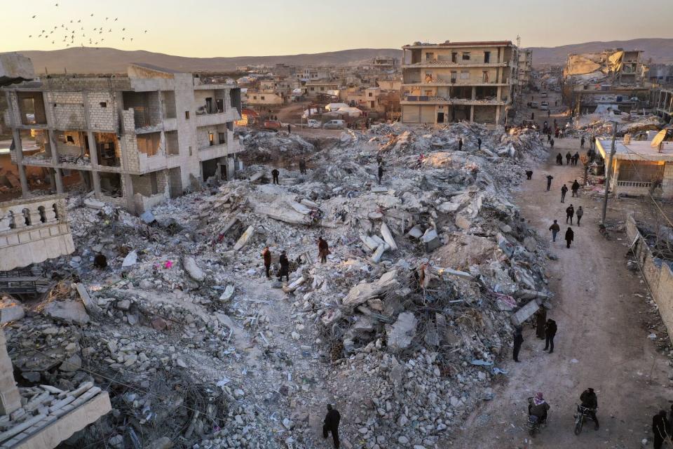 In an overhead view, people pass collapsed buildings