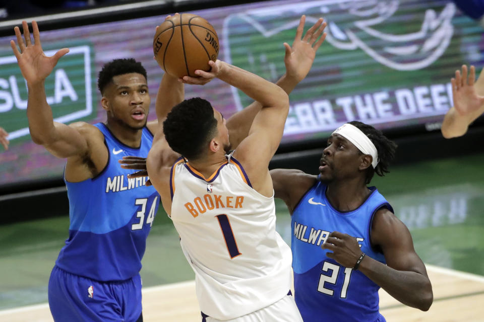 Phoenix Suns' Devin Booker, center, is fouled as he shoots between Milwaukee Bucks' Jrue Holiday, right, and Giannis Antetokounmpo, left, during the first half of an NBA basketball game Monday, April 19, 2021, in Milwaukee. (AP Photo/Aaron Gash)