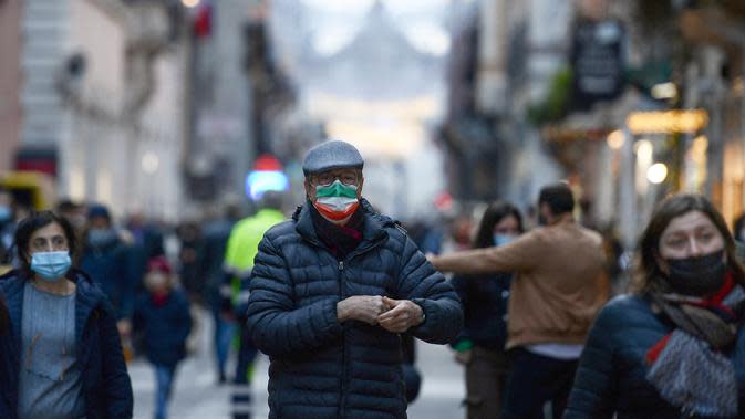 Seorang pejalan kaki, mengenakan masker dengan bendera Italia di atasnya, berdiri di jalan Roma, Kamis (23/12/2021). Pemerintah Italia telah mewajibkan kembali penggunaan masker di luar ruangan untuk menahan peningkatan kasus Covid-19 yang didorong oleh varian Omicron. (Filippo MONTEFORTE/AFP)