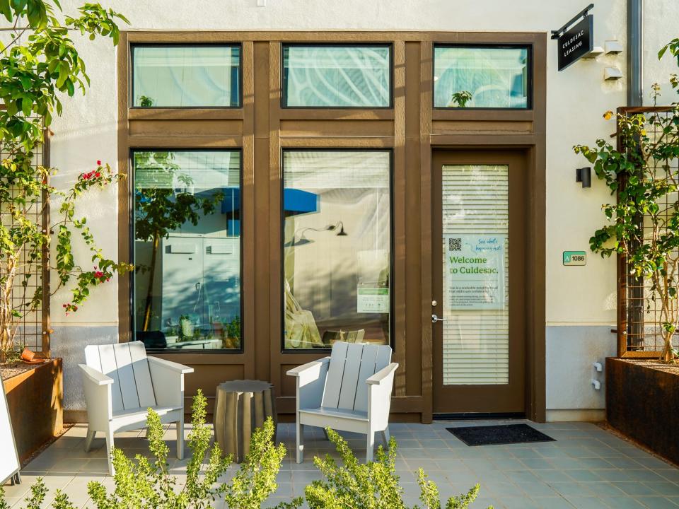 Culdesac Tempe: A white building with brown doors behind shrubbery and a small table with two chairs