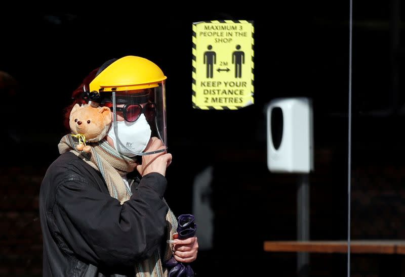 A woman wearing a face mask and a shield walks in London