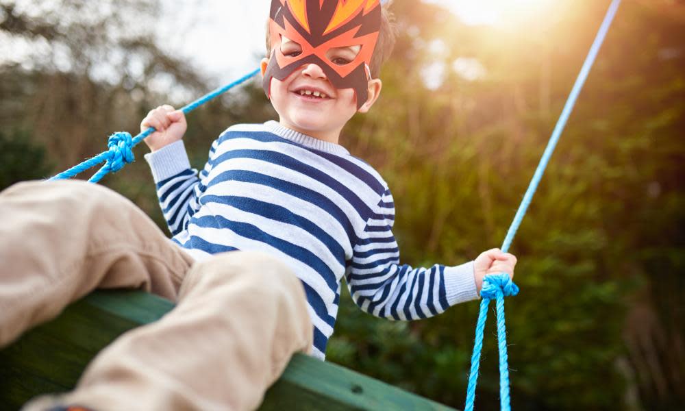 A boy playing on a garden swing wearing a mask