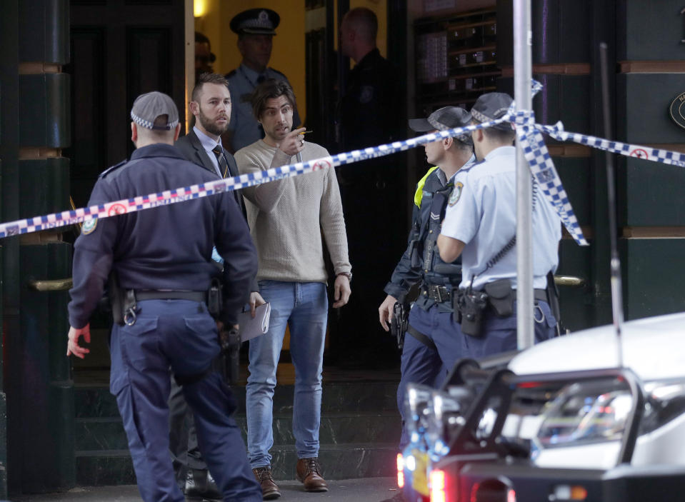 A man, center, points as he assists police at a building where a person has been found deceased after a man attempted to stab multiple people in Sydney, Australia, Tuesday, Aug. 13, 2019. Police and witnesses say a knife-wielding man yelling "Allahu akbar," or "God is great," has attempted to stab several people before being arrested, with one person taken to a hospital. (AP Photo/Rick Rycroft)