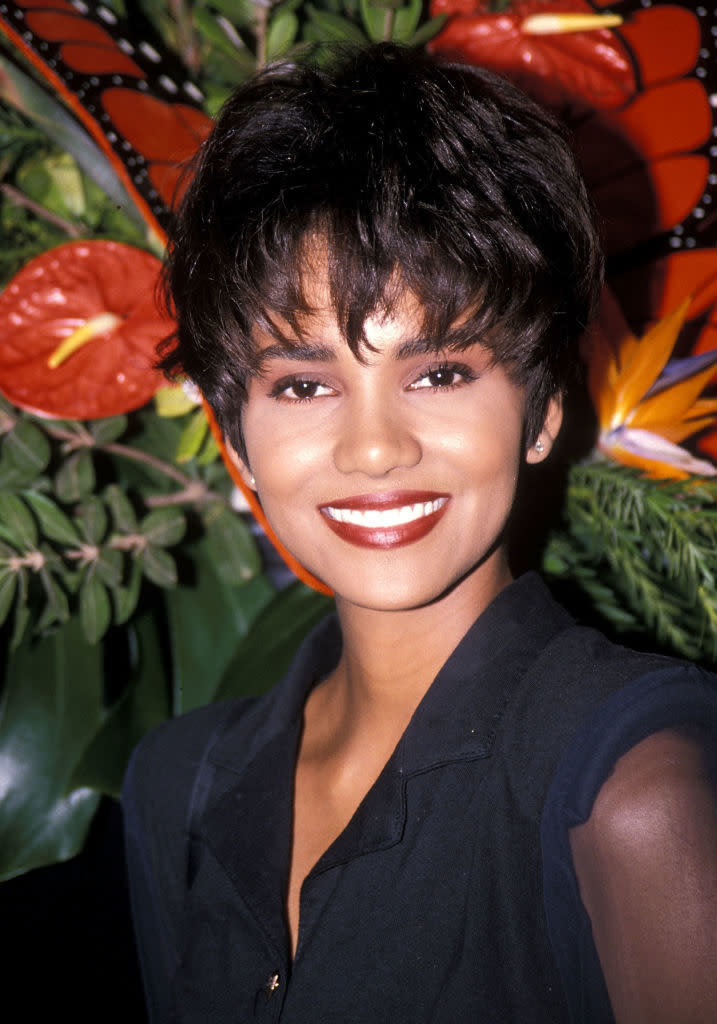 Halle with short hair in a dark blazer in front of tropical flowers