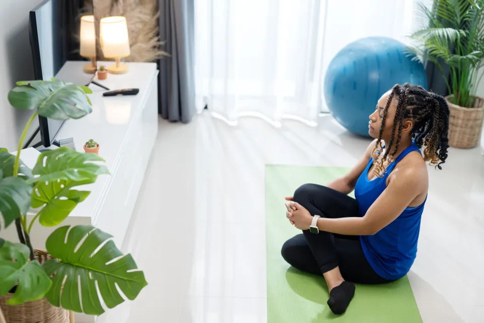 Woman sitting on a yoga mat in a home setup, preparing for or resting after a workout session