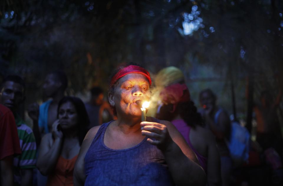 In this photo taken Oct. 11, 2019, a woman lights a cigar at the entrance of Sorte mountain to ask for permission to perform spiritual rituals where followers of indigenous goddess Maria Lionza gather annually in Venezuela's Yaracuy state. Believers congregated for rituals on the remote mountainside where adherents make a pilgrimage to pay homage to the goddess, seeking spiritual connection and physical healing. (AP Photo/Ariana Cubillos)