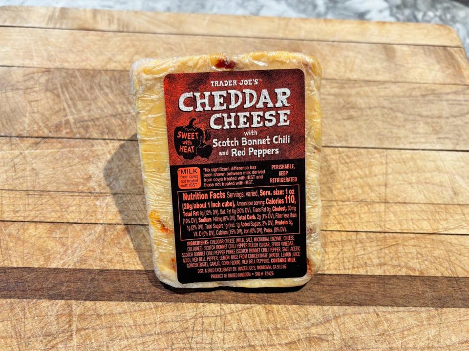 An orange wedge of cheddar cheese on a brown cutting board with a red and black label reading "cheddar cheese with scotch bonnet chili and red peppers"