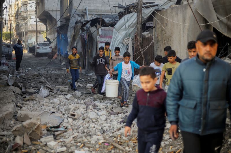 Niños palestinos llevan objetos mientras caminan en el lugar de los ataques israelíes, en Jan Yunis