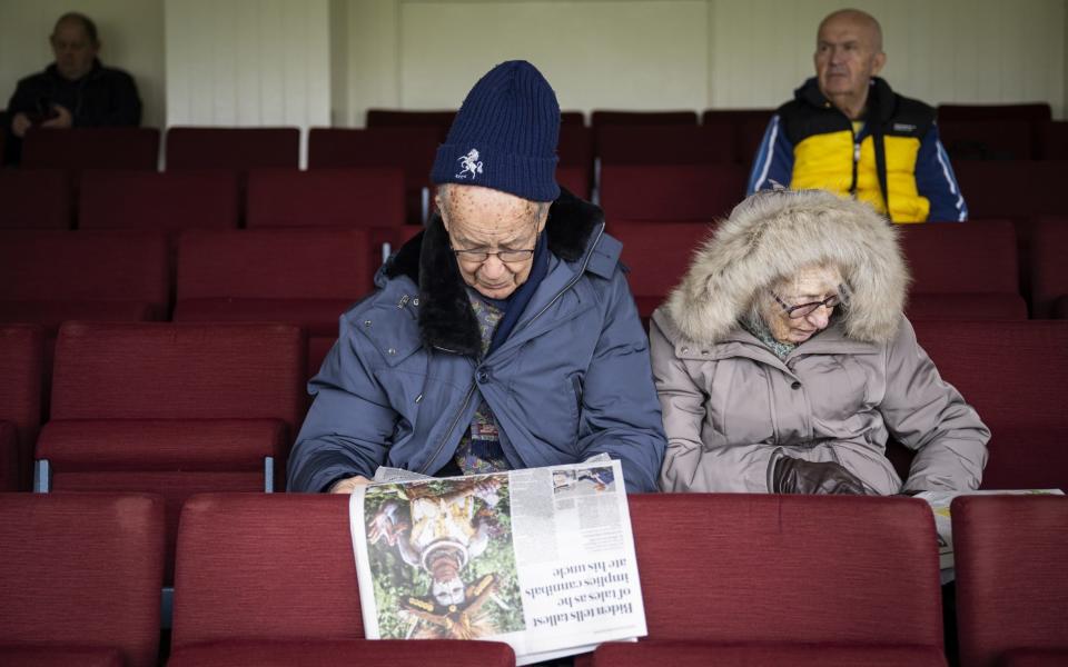 Spectators read the paper as the covers remain on as start of play is delayed for rain ahead of the Vitality County Championship match between Kent and Surrey at The Spitfire Ground on April 19, 2024 in Canterbury