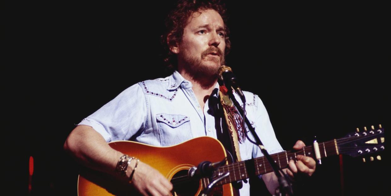 gordon lightfoot plays acoustic guitar and sings into a microphone