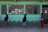 Women, wearing protective face masks and standing at a safe distance away from each other to help curb the spread of the new coronavirus, stand in line outside their children's school, in Chimaltenango, Guatemala, Friday, April 3, 2020. The parents were invited to come to the school to pick up a bag of free groceries and homework assignments for their children during a nationwide lockdown. (AP Photo/Moises Castillo)