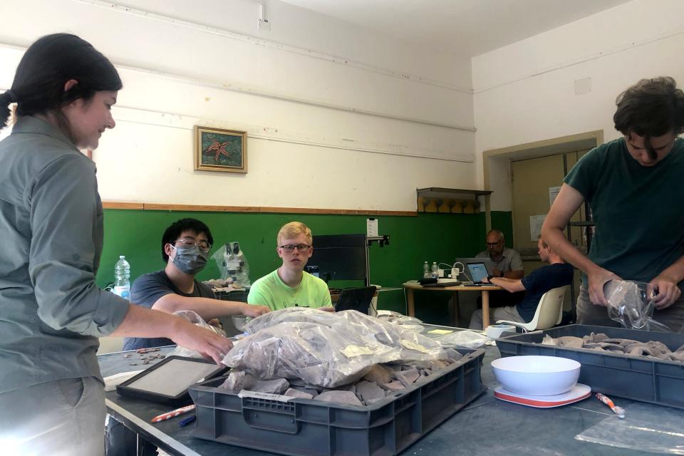 From left, Serena Crosson, Tianqi Zhu, Matt Wabler, archaeologist and site director Steven Ellis, Chris Motz, and Anna Wire analyze pottery pieces and tiles found at the site in a lab set up in an old Sardinian school.