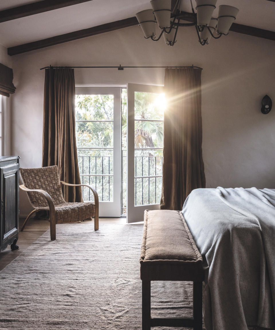 neutral beamed bedroom with bench at end of bed and wicker chair