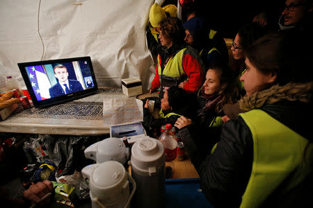 Protesters wearing yellow vests watch French President Emmanuel Macron on a TV screen at the motorway toll booth in La Ciotat, near Marseille, France, December 10, 2018. REUTERS/Jean-Paul Pelissier