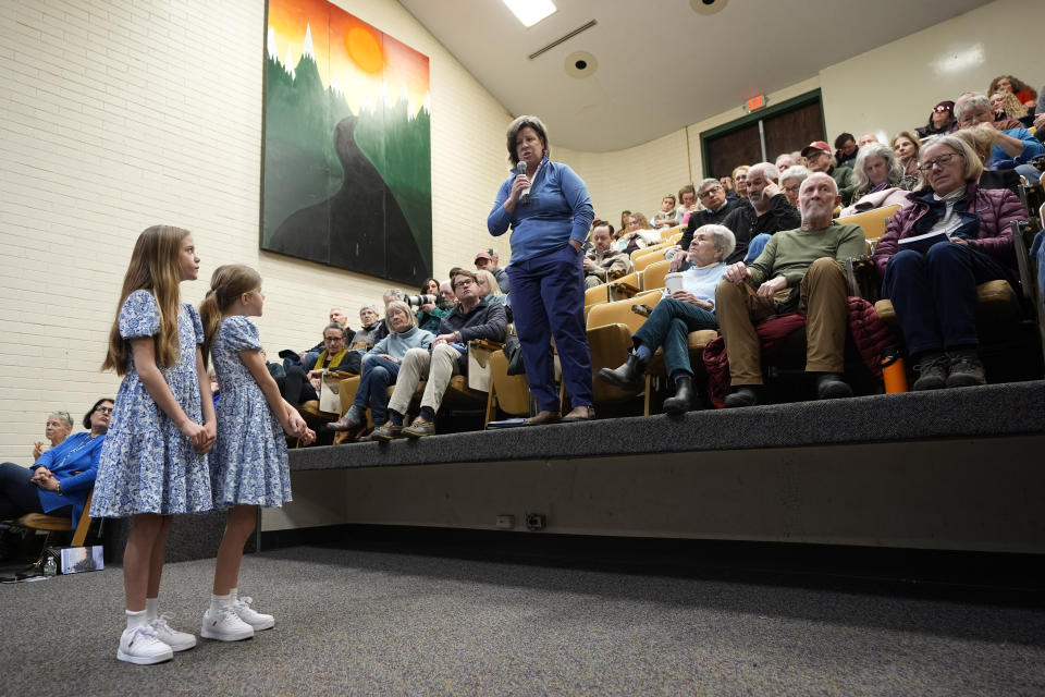 La exrepresentante estatal Heidi Scheuermann, de pie en el centro, habla durante una discusión sobre asuntos de la junta escolar en la asamblea anual del pueblo, el martes 5 de marzo de 2024, en Stowe, Vermont. Las dos niñas de la izquierda esperan para entregar el micrófono al siguiente orador. (AP Foto/Robert F. Bukaty)