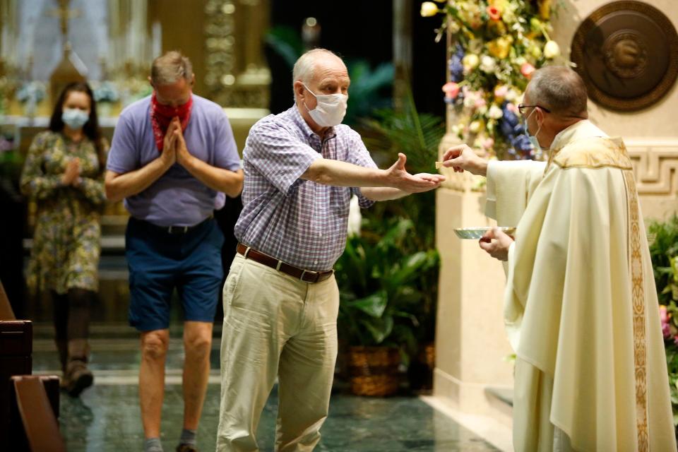 Congregation members wear face masks as they receive communion from the Rev. Jan Schmidt during a morning Mass at the Cathedral of St. Peter in Chains Catholic Church in downtown Cincinnati on May 25. The Memorial Day Mass was the first inside the church since the state-mandated stay-home order in March.