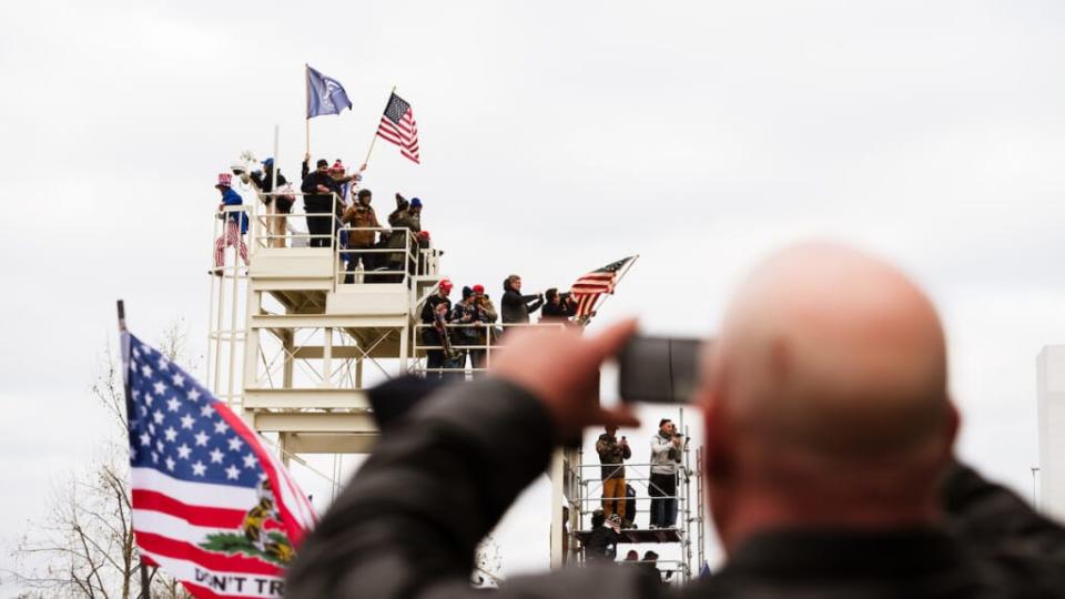 WASHINGTON, DC – JANUARY 06: A pro-Trump protester takes a photo of other protesters who climbed a media platform after breaking through barriers onto the grounds of the Capitol Building on January 6, 2021 in Washington, DC. (Photo by Jon Cherry/Getty Images)