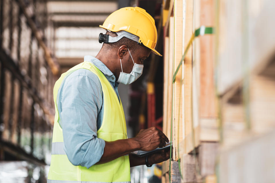 Black African worker wear protective face mask and helmet check stock in warehouse. Concept of new normal work in industry, factory after Covid 19 pandemic