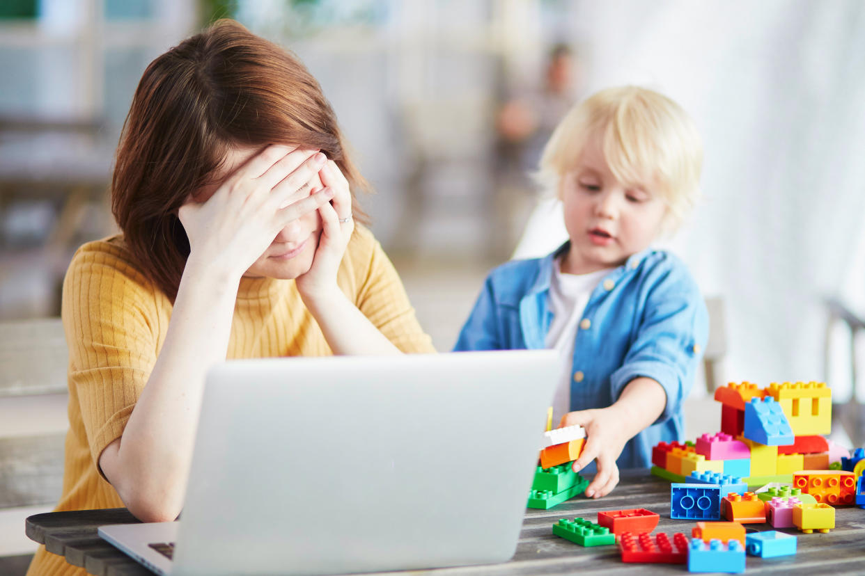 Boy playing near his tired mother working on her laptop. Quarantine and closed schools and offices during coronavirus outbreak. Homeschooling, distance learning and freelance job