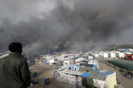 A migrant looks at burning makeshift shelters and tents in the "Jungle" on the third day of their evacuation and transfer to reception centers in France, as part of the dismantlement of the camp in Calais, France, October 26, 2016. REUTERS/Philippe Wojazer
