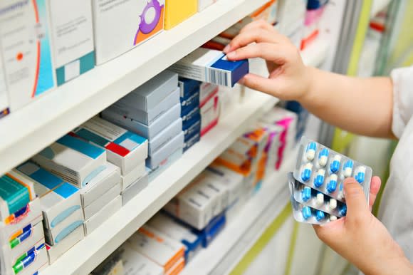 A person places medication on a pharmacy shelf.