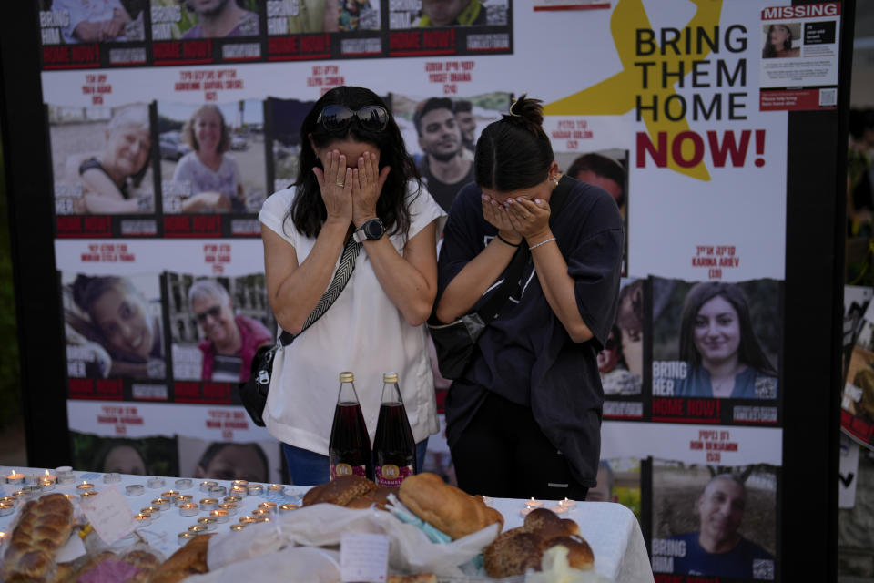 Two women pray next to photographs of people who were abducted during the unprecedented Hamas attack on Israel just before Friday dinner on the eve of Shabbath in Tel Aviv, Israel, Friday, Oct. 27, 2023. (AP Photo/Francisco Seco)