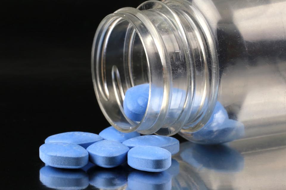 Blue pills spilled from a clear plastic container onto a surface