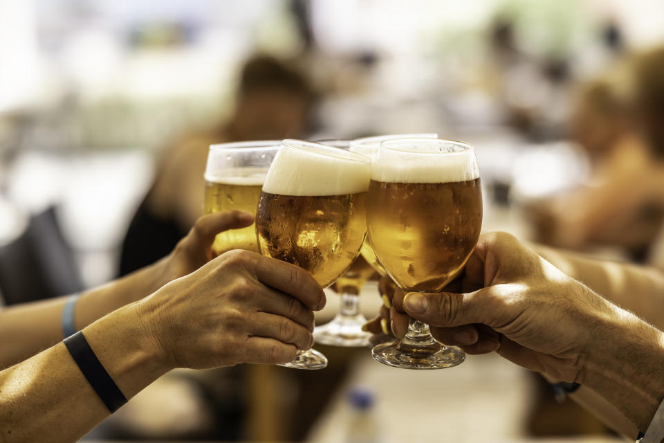 Four people clinking beer glasses together at a social gathering, possibly celebrating while traveling