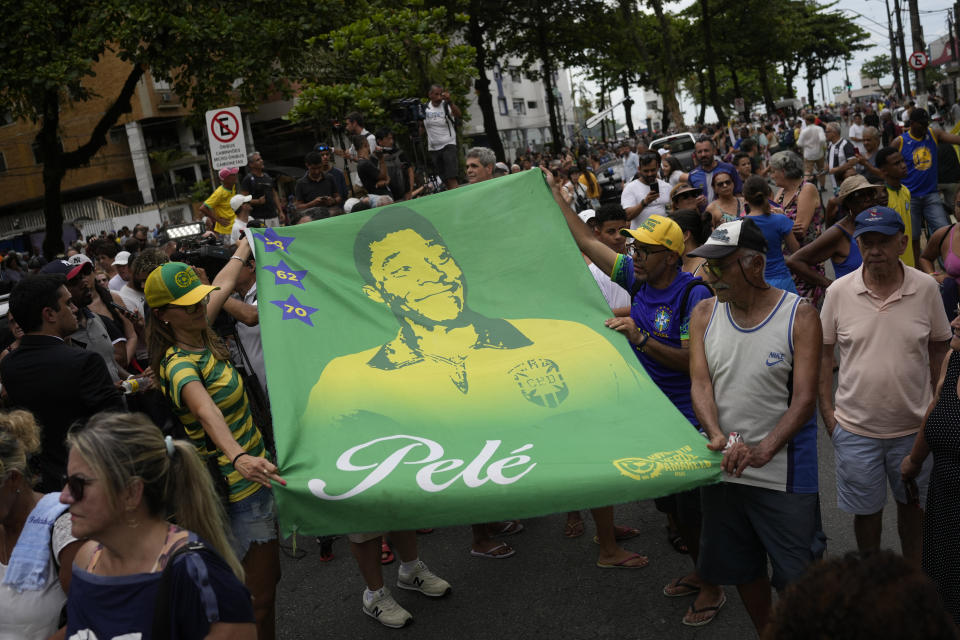People hold a banner of the late Brazilian soccer great Pele along the route of his funeral procession from Vila Belmiro stadium to the cemetery in Santos, Brazil, Tuesday, Jan. 3, 2023. (AP Photo/Matias Delacroix)