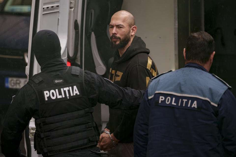 Police officers escort Andrew Tate, center, handcuffed, to the Court of Appeal in Bucharest, Romania, Tuesday, March 12, 2024. Online influencer Andrew Tate was detained in Romania and handed an arrest warrant issued by British authorities, his spokesperson said Tuesday. (AP Photo/Andreea Alexandru)