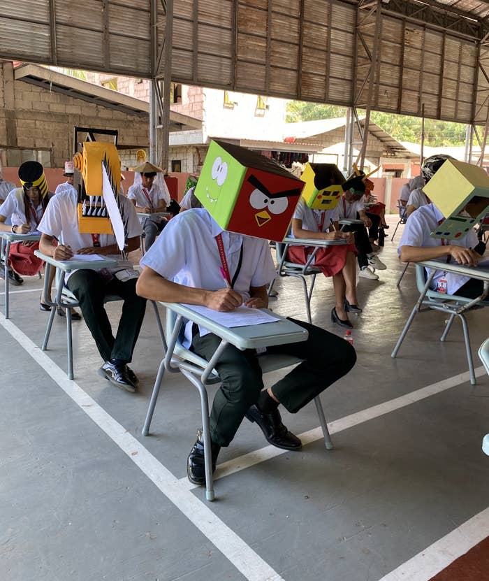 Students wearing cardboard masks of characters sit at desks in a classroom setting