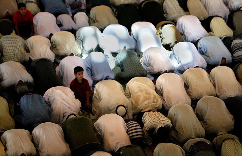 A boy sits up amid rows of people bowed over on the floor in prayer