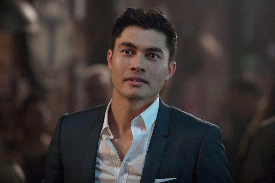 Henry Golding in a sharp suit looking pensive against a blurred background