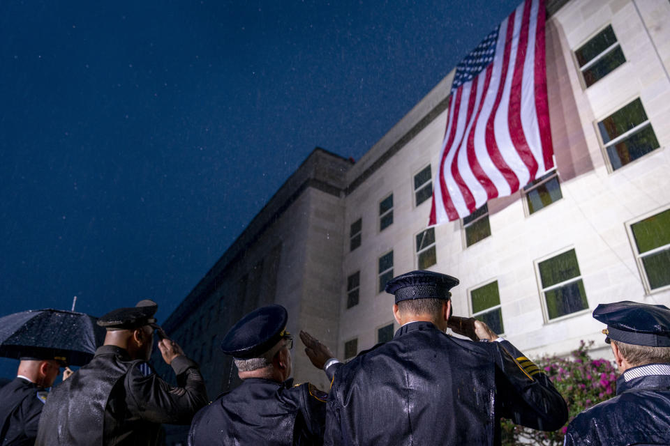 Varios policías saludan mientras una bandera estadounidense es desplegada en el Pentágono al amanecer del 11 de septiembre de 2022, en Washington, al cumplirse el 21er aniversario de los atentados terroristas del 11 de septiembre de 2001. (AP Foto/Andrew Harnik)