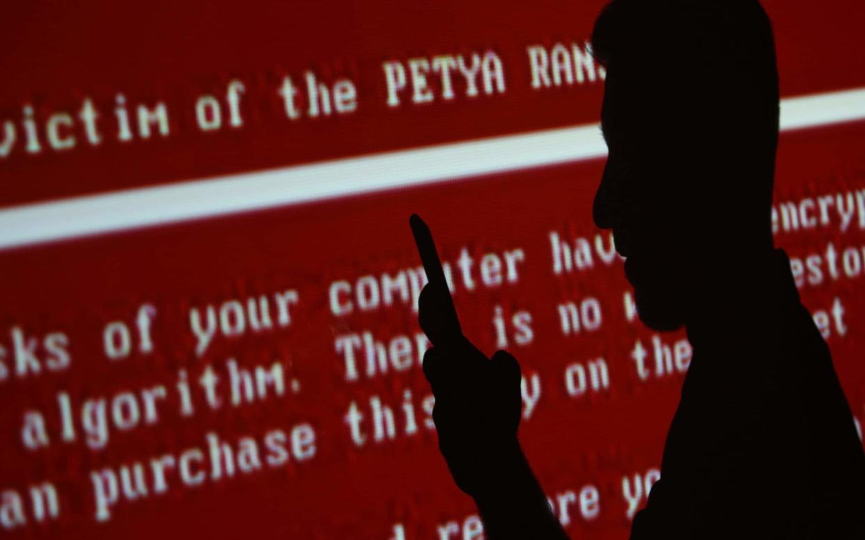 The silhouette of a young man with a mobile phone against a red background with a projected message related to the Petya ransomware - TASS