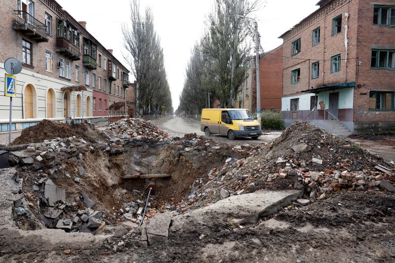 A van drives past a crater in the road caused by a missile strike, in Bakhmut