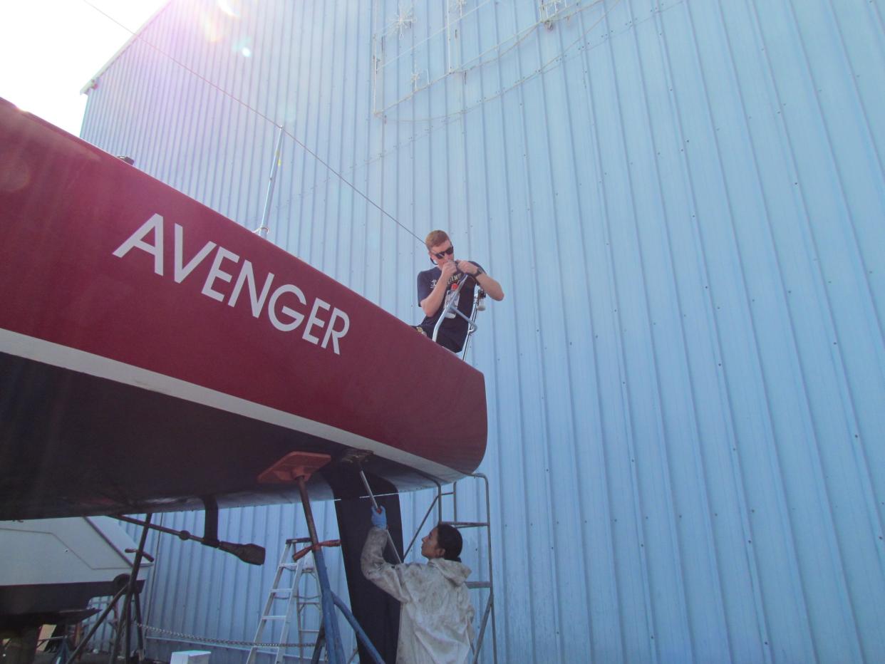 Colin Caraher tightening a safety line to the Avenger while Isabelle Navolio scrubs the hull below at Desmond Marine on July 10, 2023.