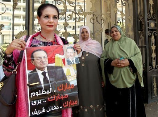 An Egyptian woman named Tahani holds a poster of ousted president Hosni Mubarak as she stands outside the military hospital where he was transfered after suffering a stroke in prison