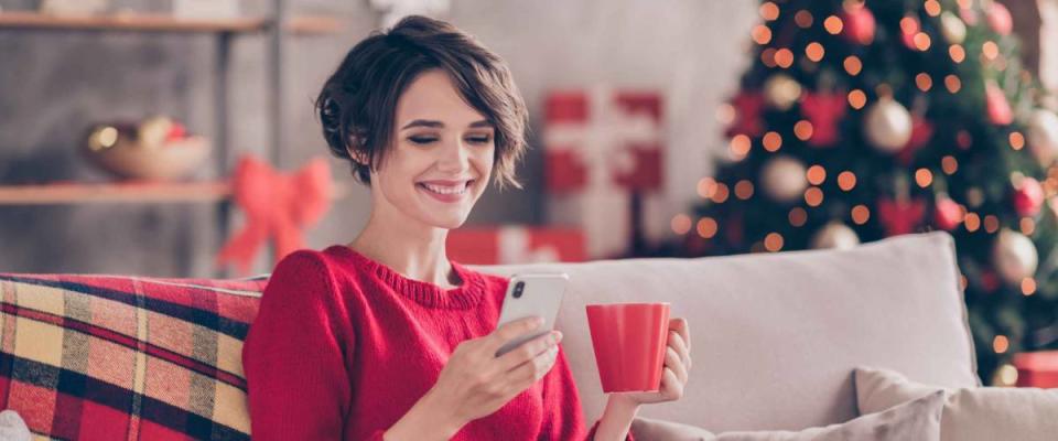 Photo of positive lady sit cozy couch use cellphone hold beverage mug in house indoors with christmas x-mas ornament