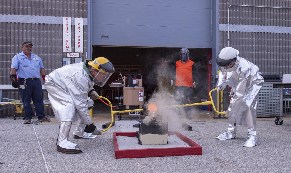 Winner of this year's Indianapolis 500 auto race, Helio Castroneves, right, pours molten bronze into a brick mold engraved with his name to commemorate his fourth winning of the race, Tuesday, July 20, 2021, at the Indianapolis Motor Speedway in Indianapolis. The brick will be laid among other bricks that mark the start/finish line of the course. Castroneves previously won the race in 2001, 2002, and 2009. Bud Tucker, a welder at the track, created the mold and assists Castroneves with the pouring. (AP Photo/Doug McSchooler)