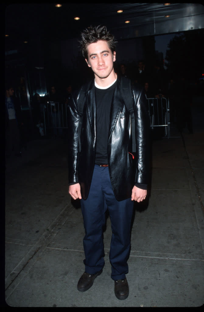 Man in leather jacket over a T-shirt with casual pants, standing on sidewalk