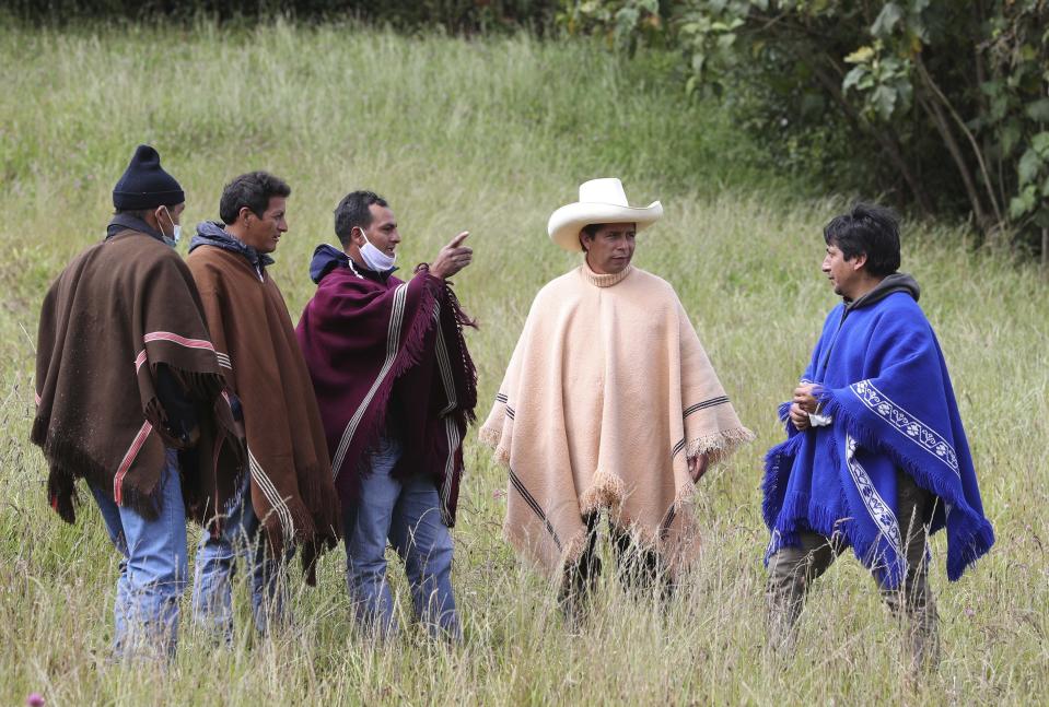 FILE - Free Peru party presidential candidate Pedro Castillo, wearing a hat and poncho, talks to neighbors in Chugur, in the Andes of Peru, April 15, 2021. When Castillo won Peru’s presidency, it was celebrated as a victory by the country’s poor — the peasants and Indigenous people who live deep in the Andes and whose struggles had long been ignored. (AP Photo/Martin Mejia, File)