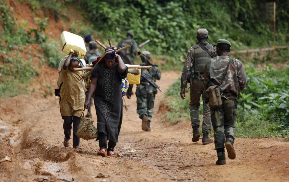 Democratic Republic of Congo (FARDC) military personnel walk past women as they patrol against the ADF and the NALU rebels near Beni in North-Kivu province