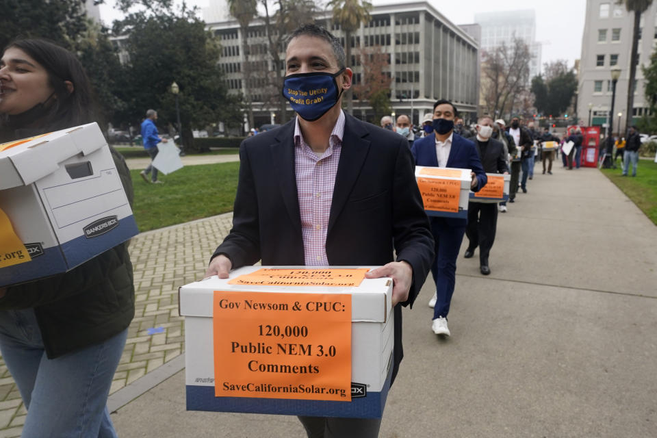 Solar energy advocates carry boxes of petitions against proposed reforms that they claim would handicap the rooftop solar market to the governor's office at the Capitol in Sacramento, Calif., Wednesday, Dec. 8, 2021. State regulators at the California Public Utilities Commission are expected to propose reforms that would lower the financial incentives for homeowners who install solar panels. (AP Photo/Rich Pedroncelli)