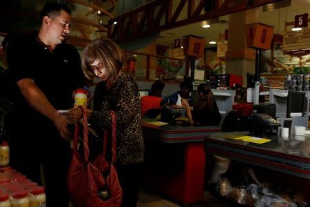 A woman receives a jar of mayonnaise and packet of pasta from a worker after she queued outside a supermarket in Caracas, Venezuela March 10, 2017. REUTERS/Carlos Garcia Rawlins