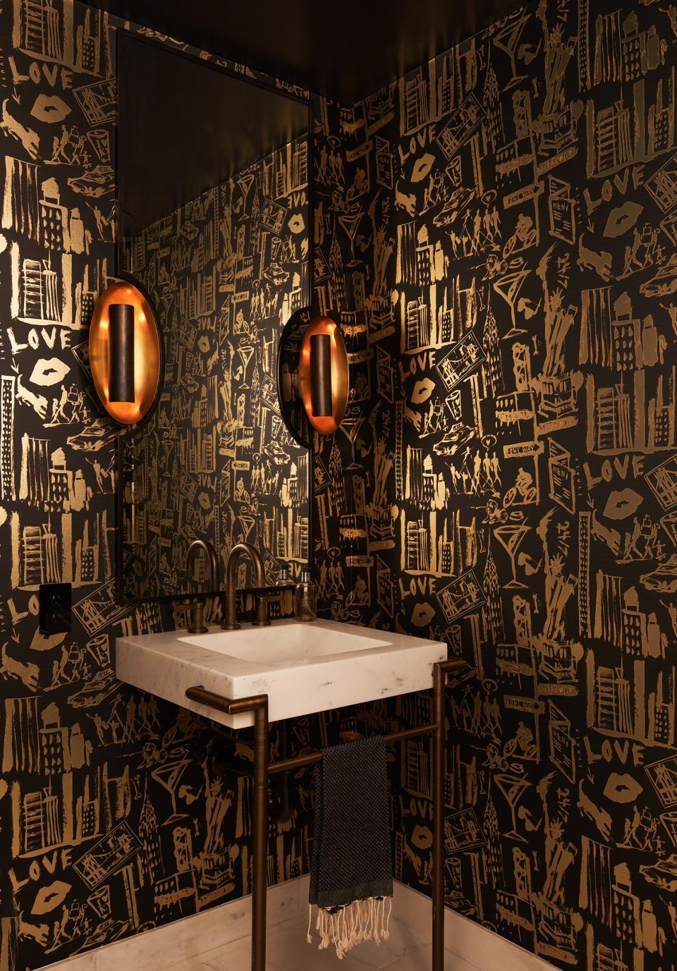 The powder room features custom wallpaper by Donald Robertson from Astek Printing. “It has references to Broadway and martinis and eating out and a dog and us. It’s sort of an homage to our life. So, that’s really special,” says Ferguson. The sconces are by Circa Lighting and the mirror is custom designed by Gurski and fabricated by Kaufman Iron Works.