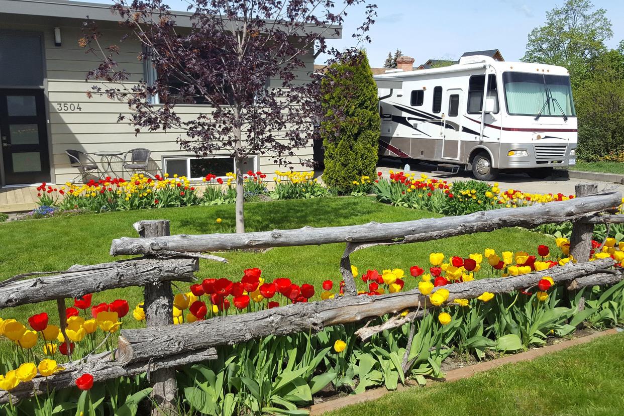 large motorhome, modest house, with red and yellow spring tulips in front yard